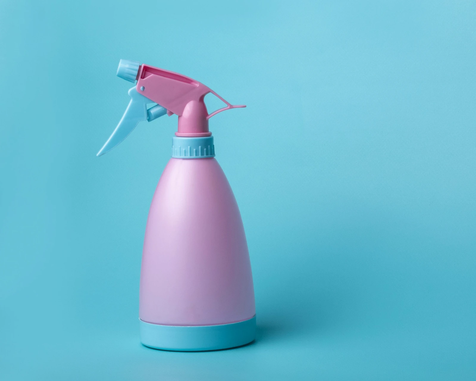 A pink-and-white trigger spray bottle against a blue background, illustrating household cleaning products; not a Meitar product.
